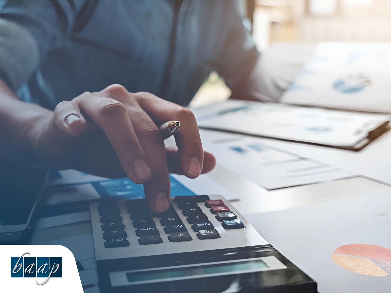 Close-up of a person using a calculator with financial charts and business documents in the background